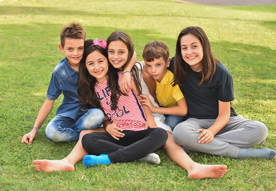 foto di un gruppo di bambini e bambine abbraciati sul prato che sorridono, scatatta da Ferruccio Munzittu