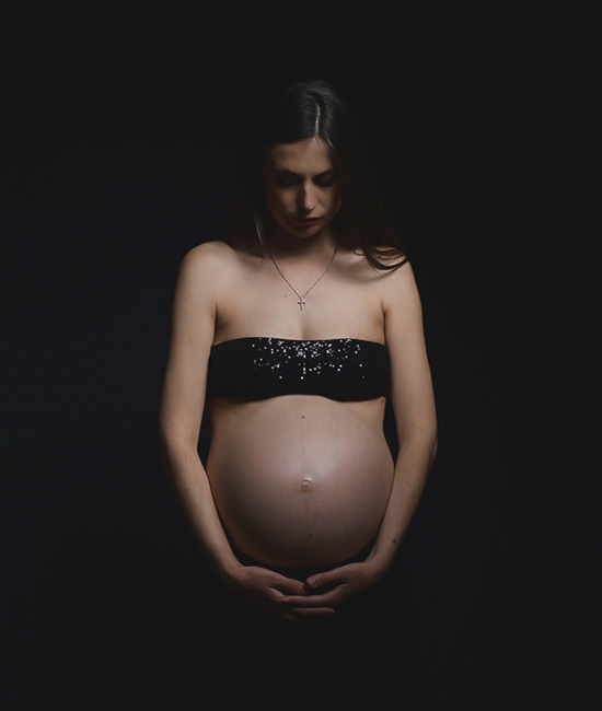 Foto artistica di donna incinta con il pancione con testa bassa e occhi chiusi, in low-key, scattata in studio da Ferruccio Munzittu